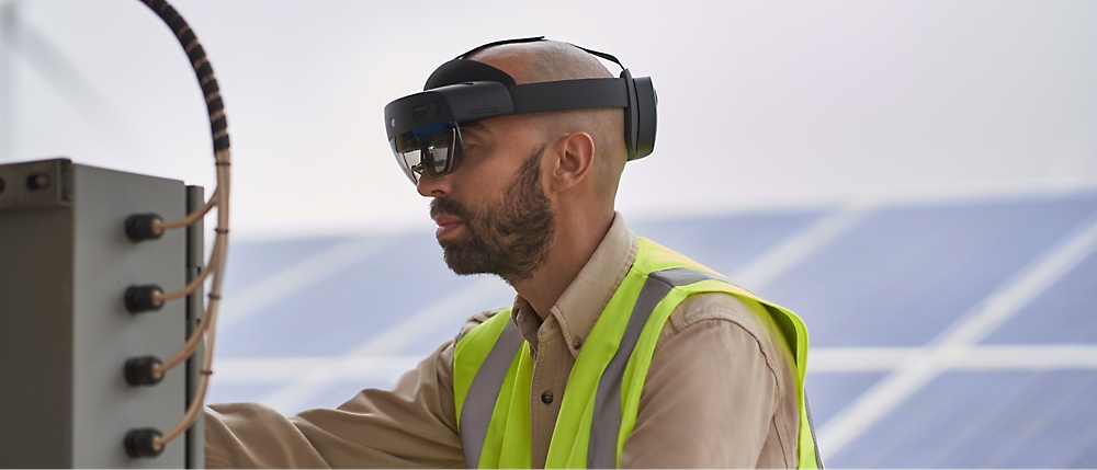 Egy láthatósági mellényt és kiterjesztett valóság headsetet viselő személy a szabadban kezel egy vezérlőpanelt. 