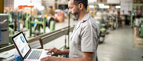 A man working on a laptop in a factory.