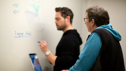 Two people talk while one of them writes on a whiteboard.