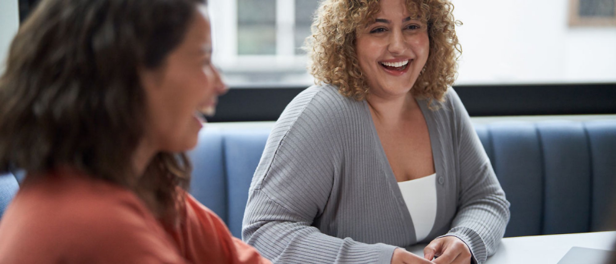 Two woman sitting in office, talking and smiling