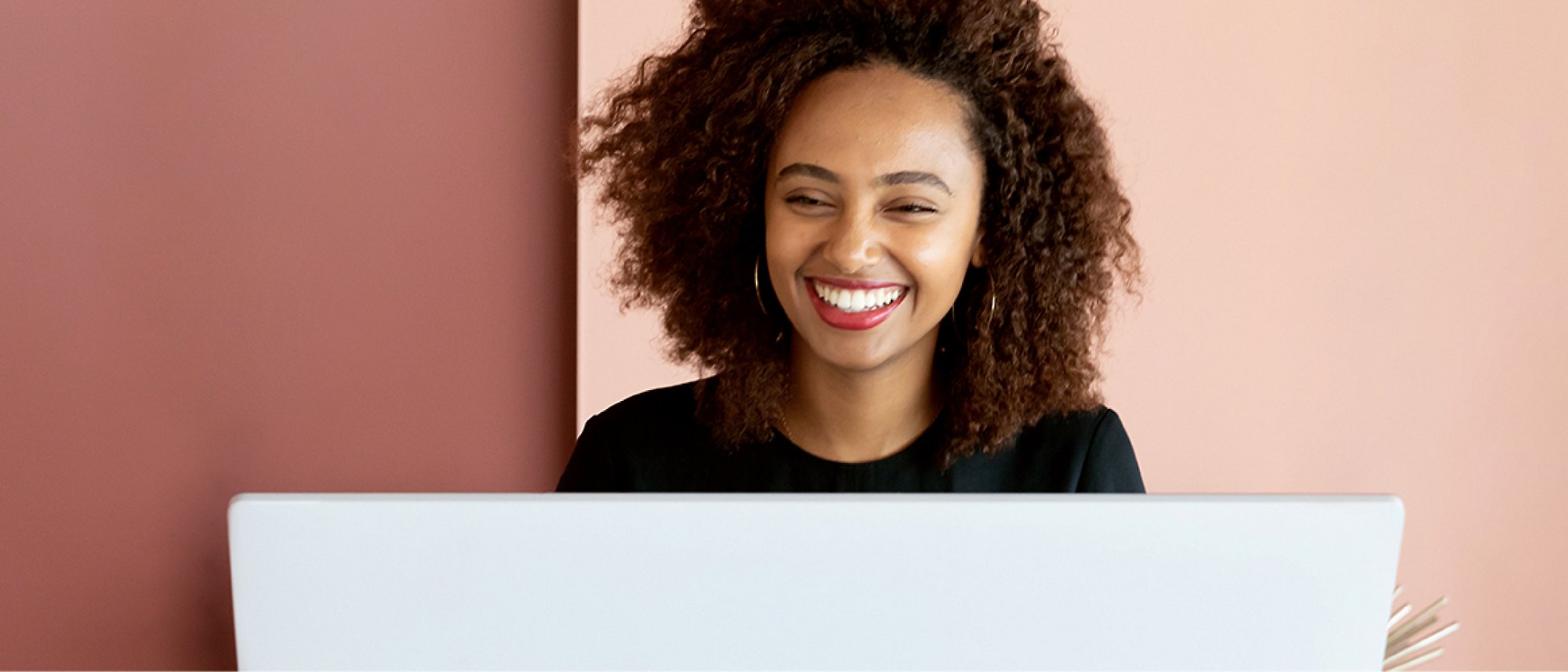 Een vrouw die lacht en op haar laptop werkt