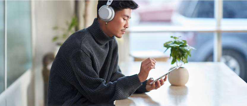 A man wearing headphones is sitting at a table with a tablet.