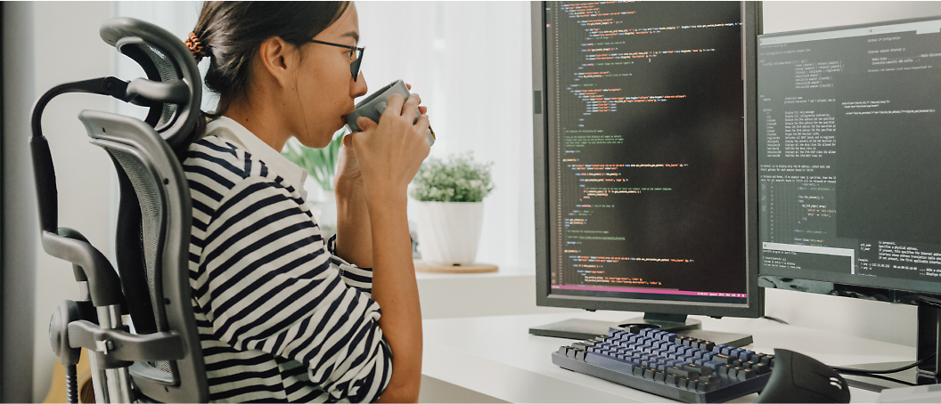 A female is consuming coffee while working on a desktop.