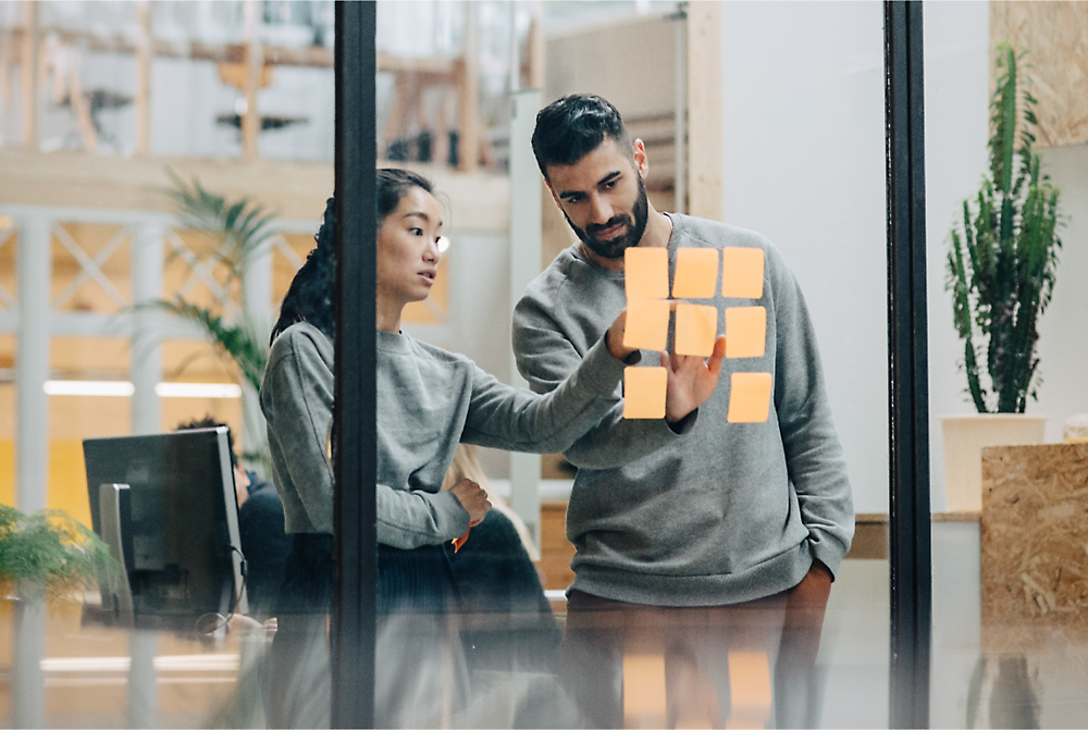 Dos personas mirando notas adhesivas en una pared de cristal