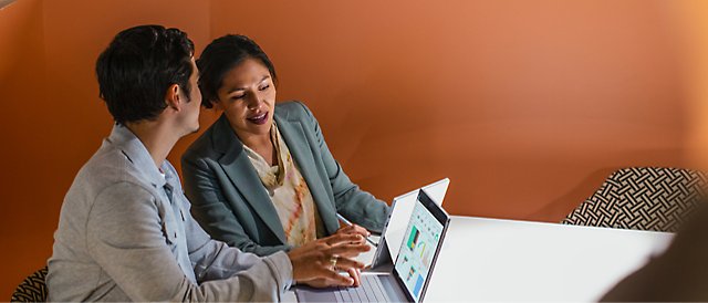 Two persons discussing while working on their laptops