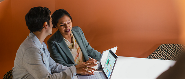 Two people sitting at a table with a laptop in front of them and discussing