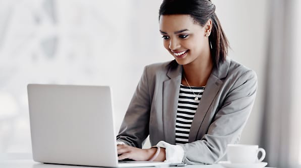 A person is sitting at a desk, smiling while using a laptop.