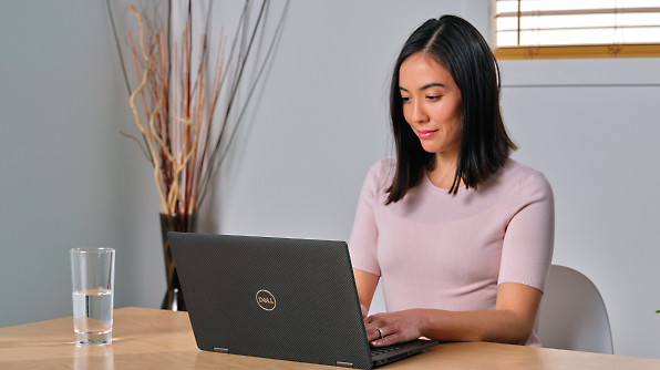 A woman sits at a desk typing on a Dell laptop. 