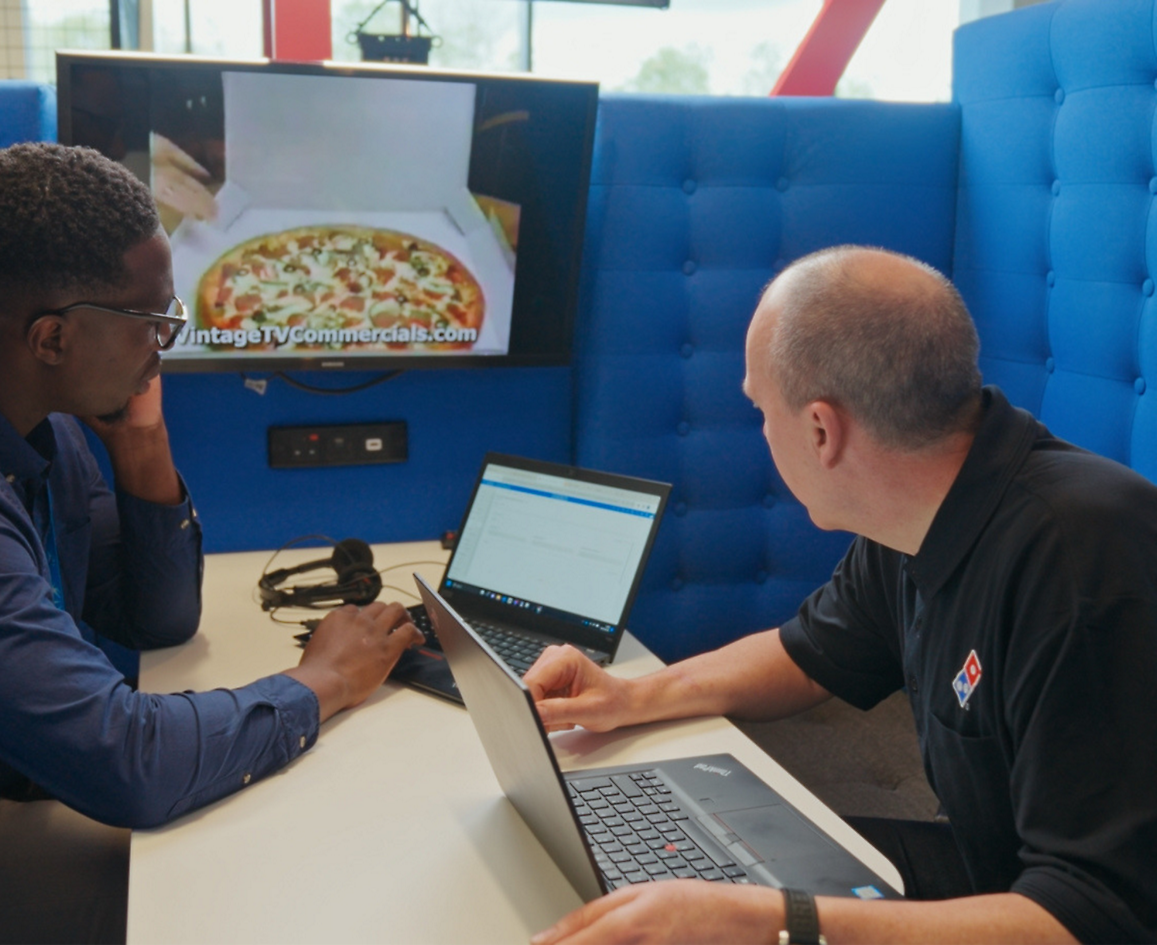 两个人坐在笔记本电脑旁讨论达美乐比萨