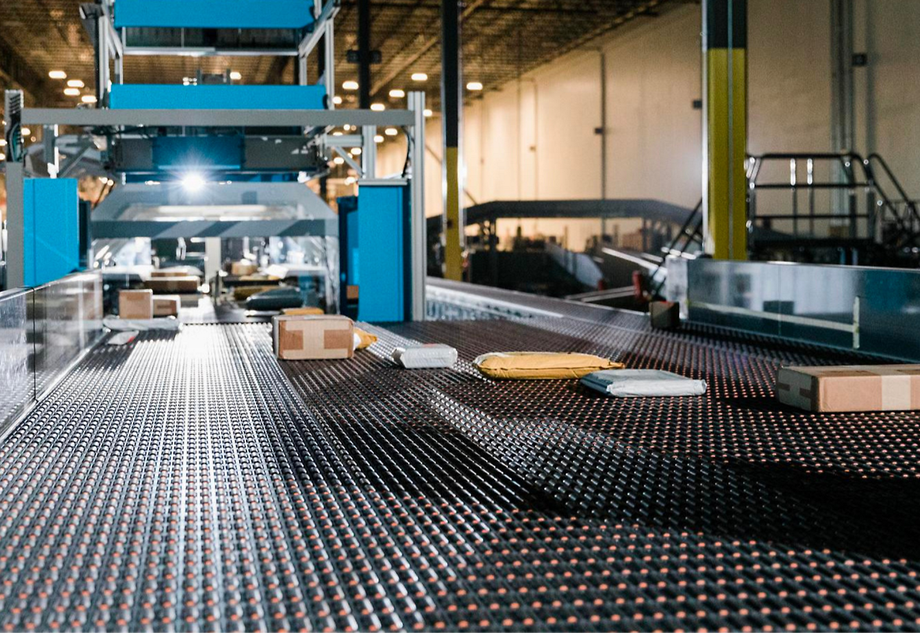 A conveyor belt carrying various packages in a warehouse, with machinery 