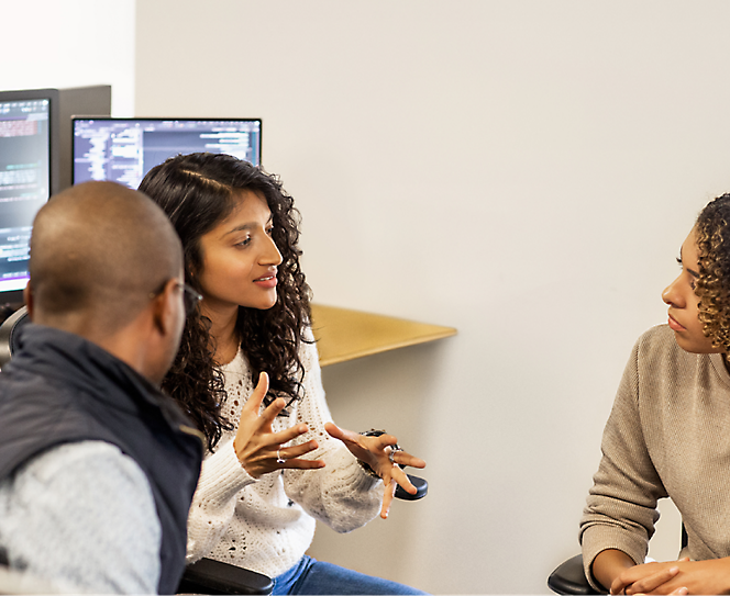 A group of people having a discussion with desktops open in the background.