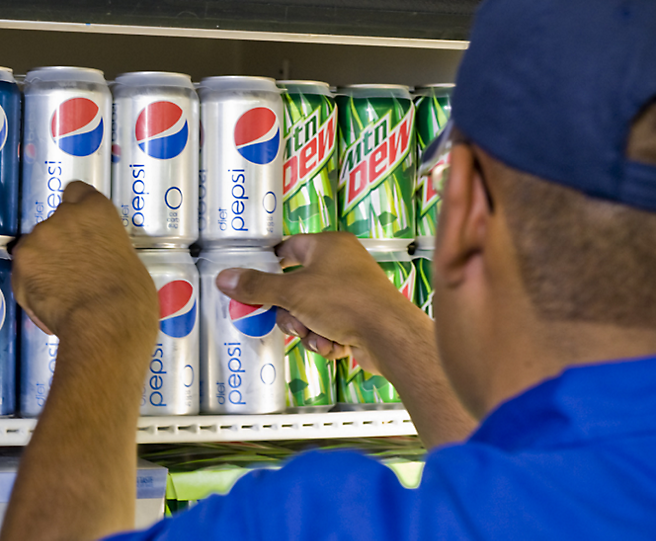 Ein Mann in einem blauen Hemd, der eine Dose Pepsi hochhebt.