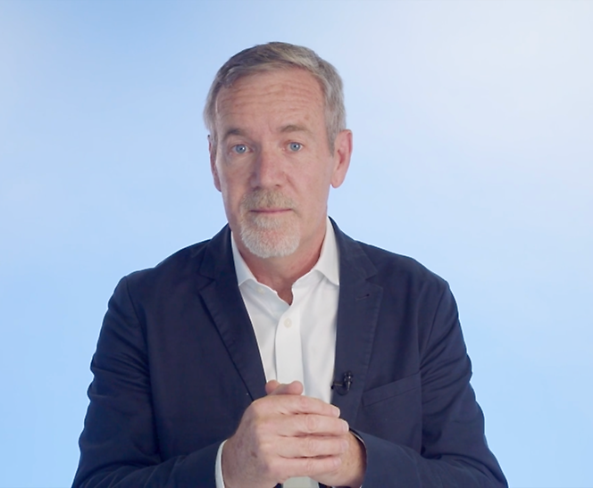 A man with a beard is standing in front of a blue background.