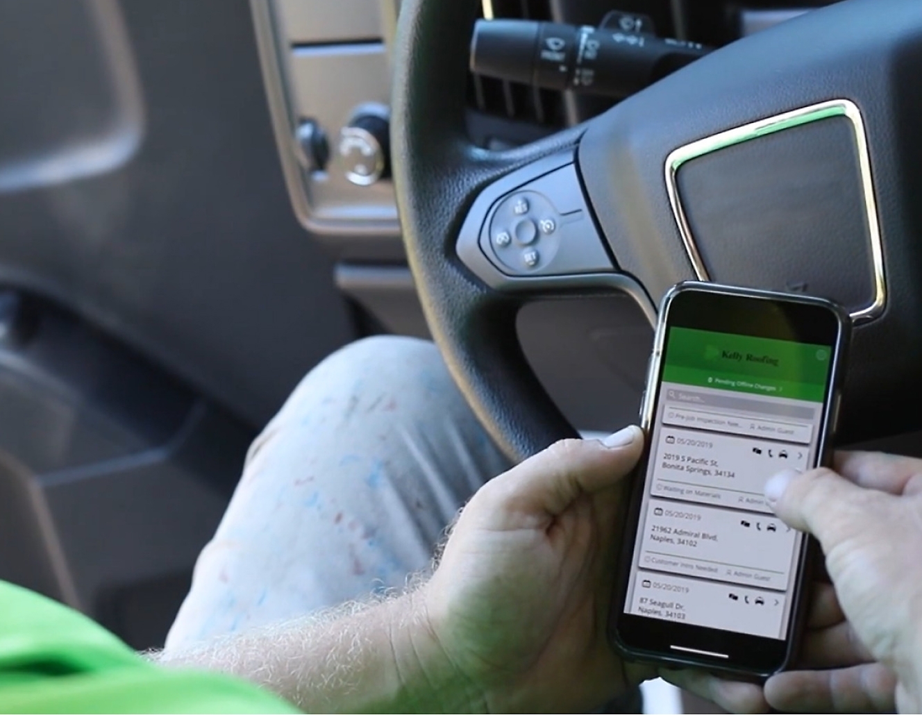 אדם עם בחולצת טריקו ירוקה משתמש בטלפון סלולרי בעת נהיגה במשאיות.