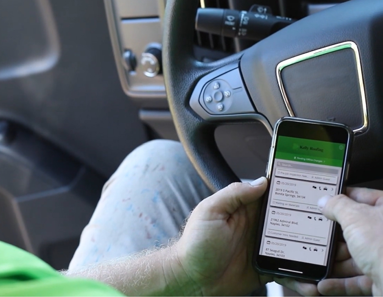 A man in a green tee is using a cell phone while driving a truck.