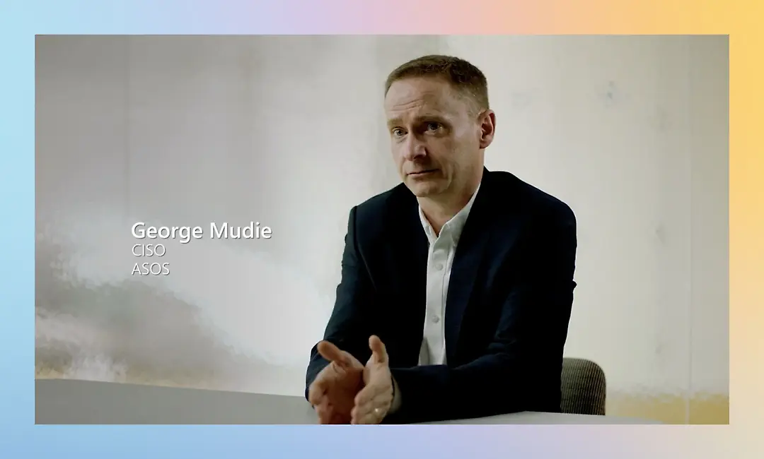 A man in a dark suit sits at a table looking forward, with the text "George Mudie, CIO, ASOS"