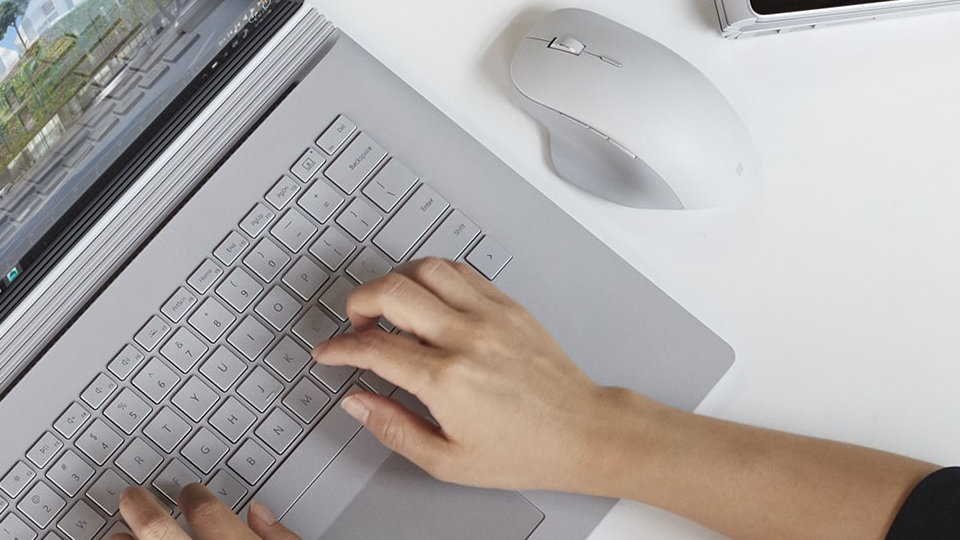 Fotografie zařízení Surface Book vedle myši Surface Precision Mouse.