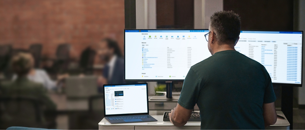 Person working on a computer with dual monitors and a laptop, displaying spreadsheets and applications