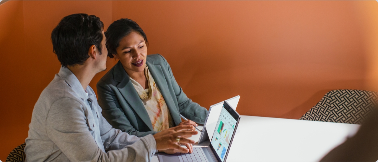 Two people in a meeting discussing content on their laptops. One person is pointing at a screen