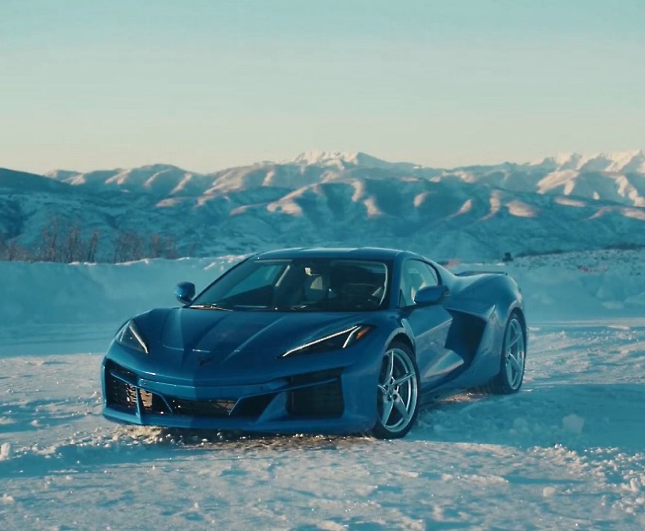 A blue sports car parked on a snow-covered terrain with mountains in the background