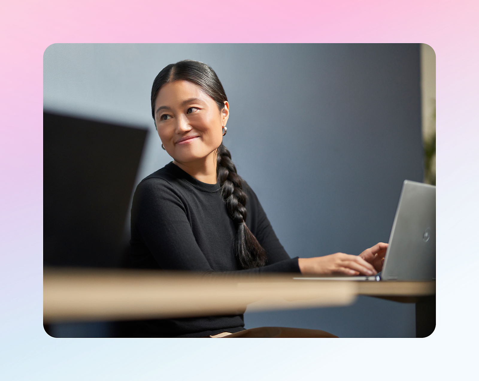 A person with a long braided hairstyle is looking to the side while using a laptop in a softly lit room.