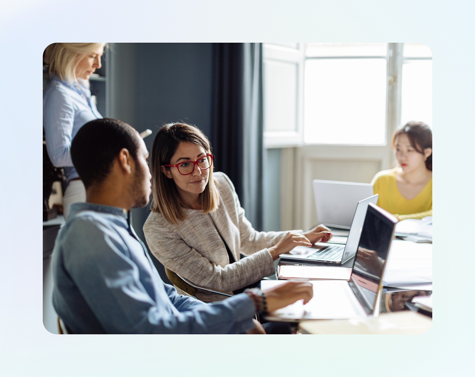 A group of four people working together in a casual office setting. Two are engaged in a conversation, one is writing