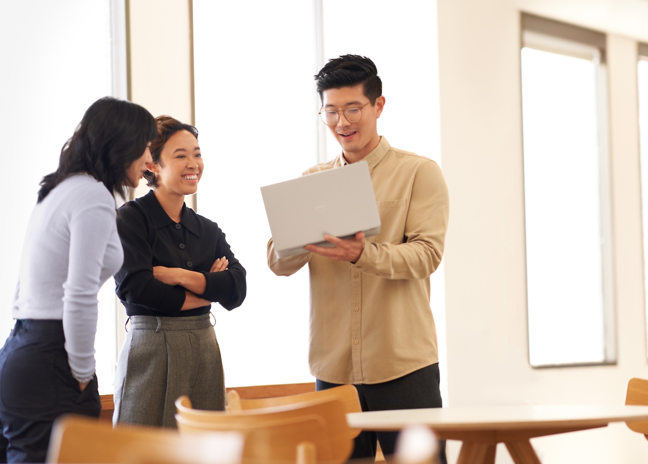 Three people stand together indoors, looking at a laptop held by one of them and smiling.