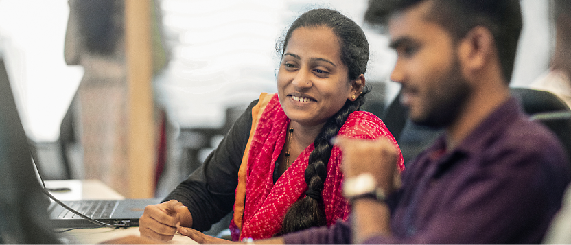 Two people in an office working, looking at the desktop and smiling.