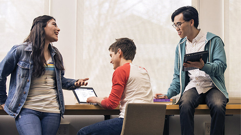 Skupina vysokoškolských studentů, kteří používají zařízení Surface a vedou přátelskou konverzaci.