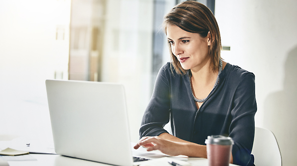 A woman sits at a desk, working on a laptop with a focused expression