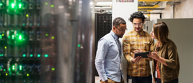 Three people in a server room looking at a computer.