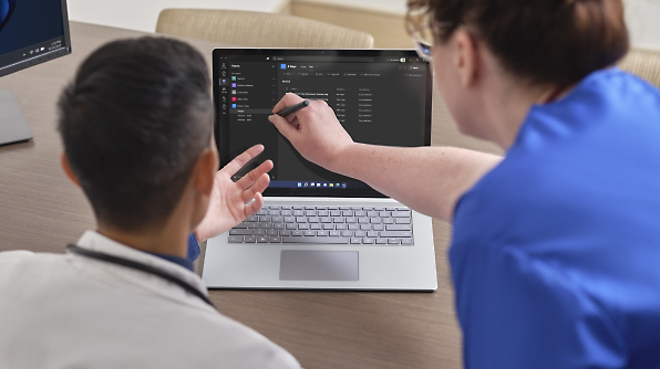 Two individuals, one with a stylus, collaborate in front of a laptop displaying a dark-themed file management application.