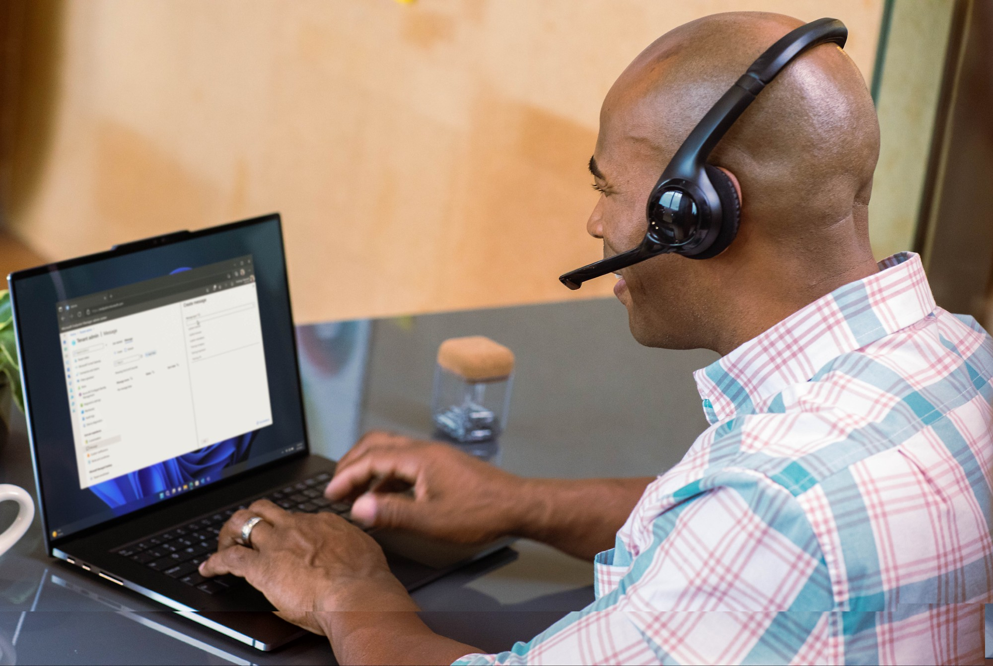 A person wearing a headset sits at a desk, typing on a laptop.