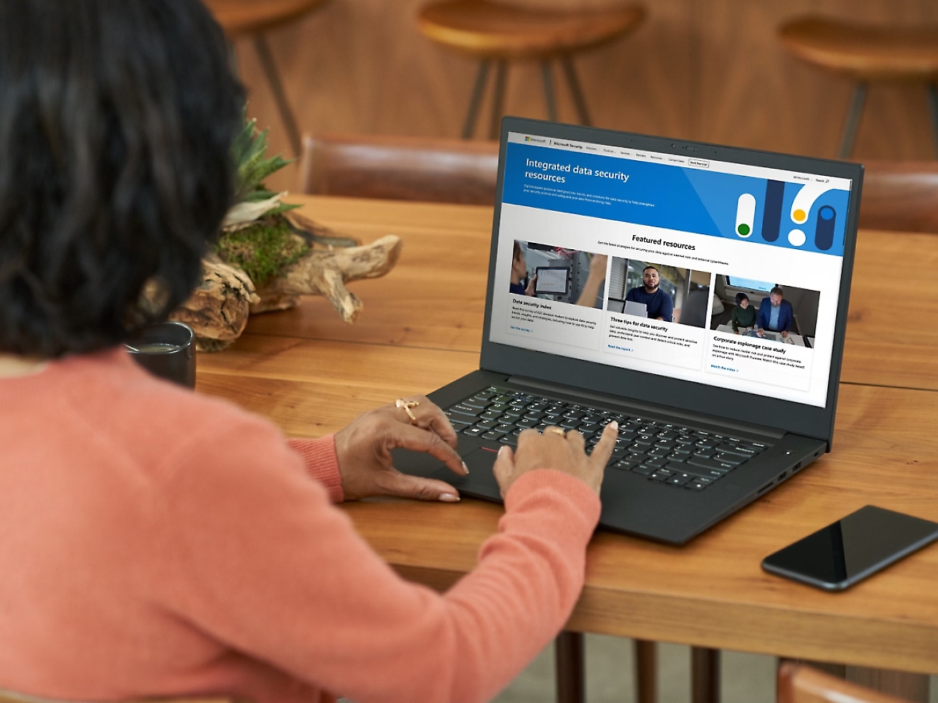 Woman in orange sweater using laptop displaying a website about data security on its screen at a wooden table