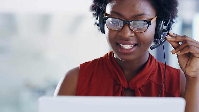 A person wearing glasses and a headset is looking at a screen while talking, with a blurred background.