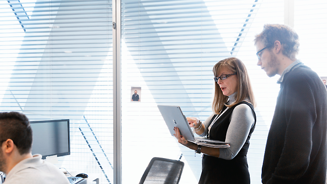 Two professionals review content on a laptop screen in a modern office setting.