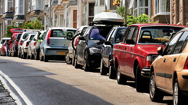 Véhicules garés le long d’une rue animée avec leurs rétroviseurs latéraux dépliés.