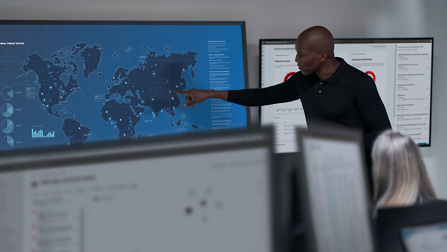 A person pointing to a world map on a wall and speaking to a colleague