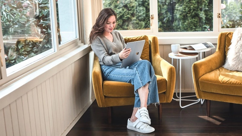 Eine Frau sitzt mit einem Laptop auf einem Sessel.