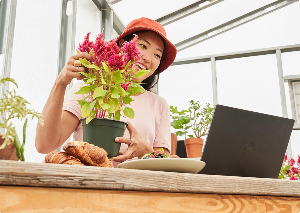 O femeie care îngrijește o plantă și privește la laptop