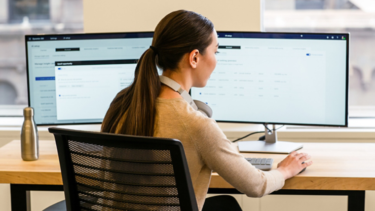 Eine Person arbeitet in einem Büro an ihrem Laptop sowie an zwei Monitoren und einer Maus