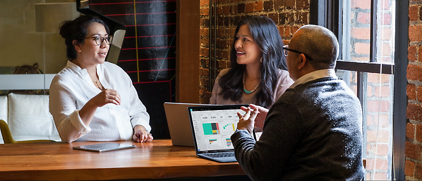 Three people engaged in a discussion at a table in a brick-walled office