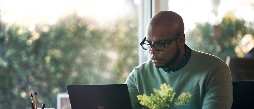 A man working on a laptop in front of a window.