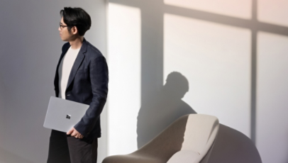 Surface Laptop 13.8 インチ (カラー: プラチナ) を閉じた状態で持ち運ぶ人物。