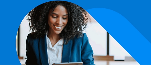 A smiling person with curly hair wearing a blue blazer and white shirt looks at a tablet.