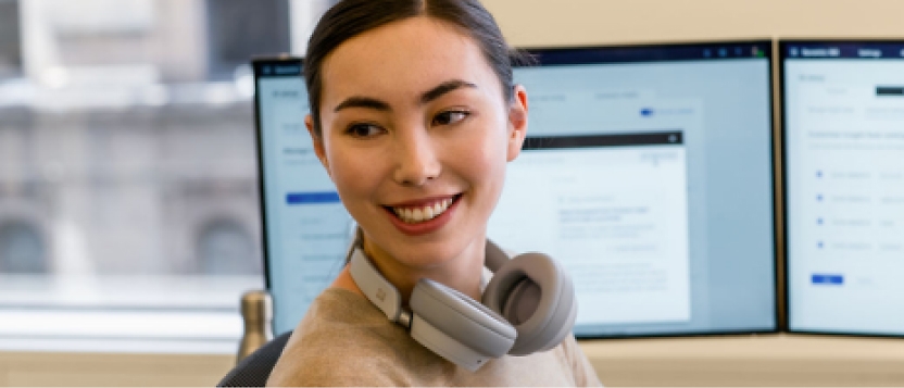 A woman wearing headphones in front of two monitors.