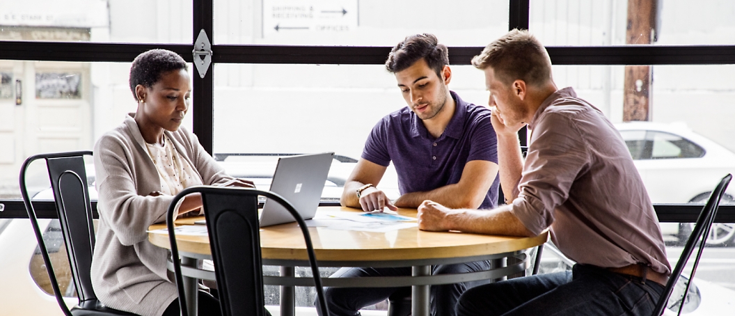 Three person are sitting in an office and discussing with one of them using a laptop