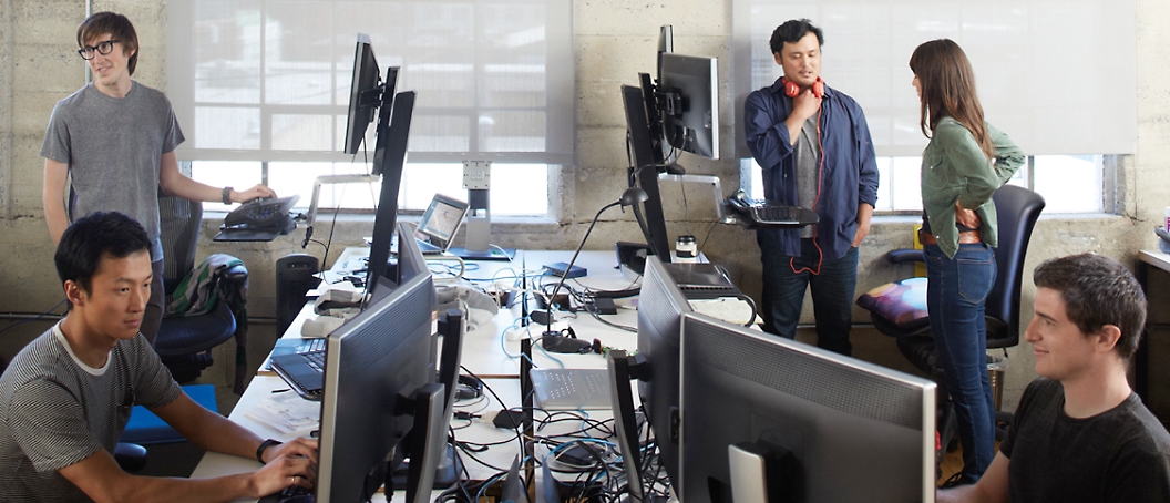 A group of people in an office working on desktop computer and discussing