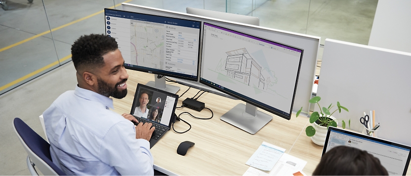 Two people working at a desk with two monitors.