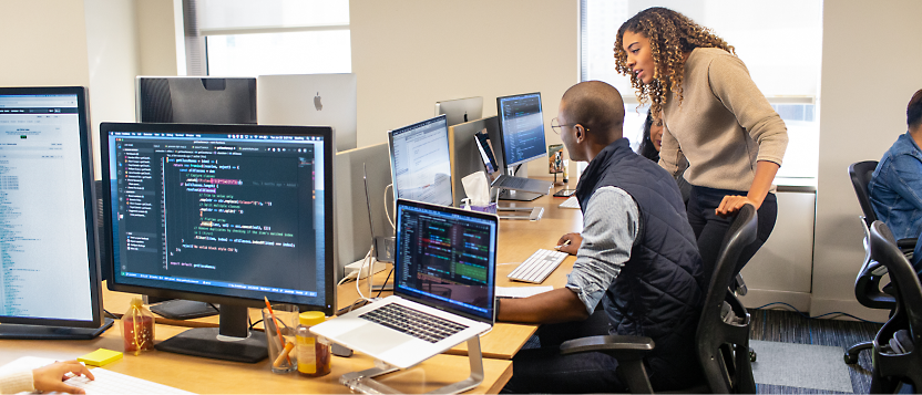 A person and another person sitting at a desk with computers